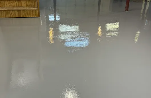 Industrial-grade high-gloss solid color epoxy flooring reflecting overhead lights in a clean commercial workspace.