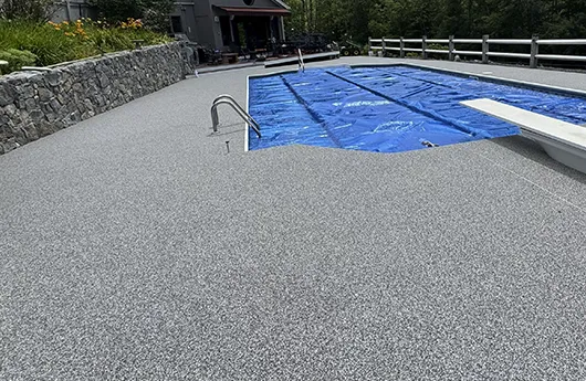 Seamless grey stone carpet flooring installed on a residential pool deck, providing a slip-resistant and elegant surface.